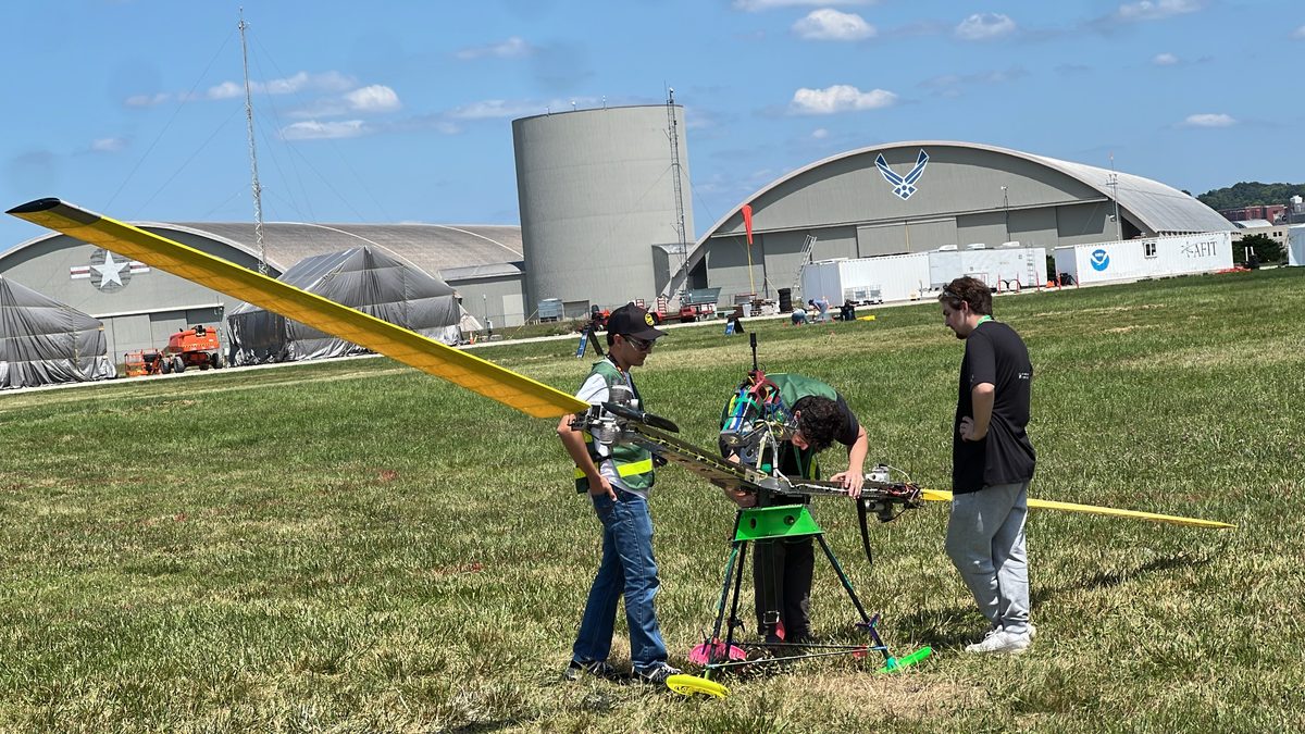 Team members preparing Stella 2 in a field, with one long yellow rotor blade in the foreground
